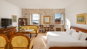 Une chambre d’hôtel avec un lit, une télévision, une table à manger avec des chaises, un mur en pierre et une vue sur la mer.