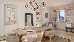 Un coin repas avec une table en bois, quatre chaises, un lustre et un mur en pierre agrémenté d’une fenêtre.