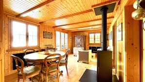 A wooden interior with a round dining table, chairs, a fireplace, and a large window. - Exclusive Chalet with amazing view (Benken)