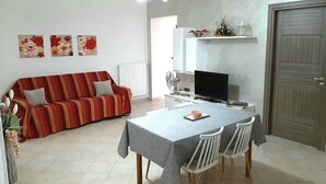 Un soggiorno con divano, tavolo da pranzo e sedie, televisione e una porta.