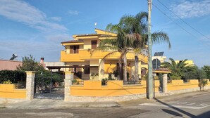 Un edificio residenziale giallo a più piani, con un cancello, un piccolo portico e una palma.