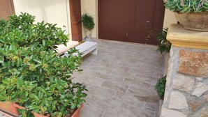Un cortile con pavimento in pietra, una porta marrone e piante in vaso.