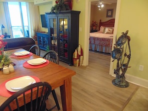 Un comedor con una mesa de madera dispuesta para dos personas, un armario azul y una habitación visible a través de una puerta abierta.