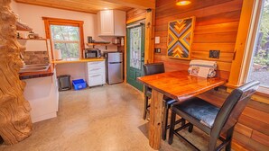 A cozy cabin-style kitchen with a wooden table and chairs, a refrigerator, microwave, and a sink. - #3 CABIN COUPLES KING BED HOTTUB BEACH (Ucluelet)