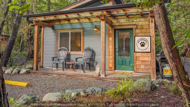 A cabin with a porch, two chairs, a table, and a pet-friendly sign. - #3 CABIN COUPLES KING BED HOTTUB BEACH (Ucluelet)