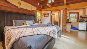 A cozy bedroom with a large bed, wooden ceiling, and a surfboard on the wall. - #3 CABIN COUPLES KING BED HOTTUB BEACH (Ucluelet)