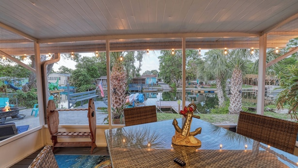 An outdoor dining area with a glass table, wicker chairs, and a view of a pool and greenery. - Waterfront w access to the Weeki Wachee River & Gulf of Mexico - Dog Friendly! (Spring Hill)