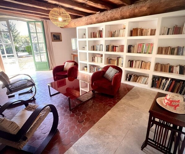 Un salón acogedor con una mesa de centro de vidrio, dos sillones rojos, una estantería llena de libros y una mesa de comedor de madera con un pastel.