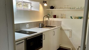 Una cocina compacta con gabinetes blancos, un lavamanos de acero inoxidable y un horno empotrado.
