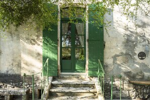 A rustic wooden door with green shutters, a stone staircase leading up to it, and a small table beside the door.