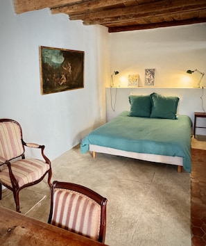 Un dormitorio con una cama, dos sillas, un cuadro y un escritorio.