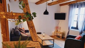 Una sala de estar acogedora con vigas de madera a la vista, un televisor de pantalla plana, un sofá, una mesa de centro y un helecho en maceta.