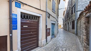 Une ruelle étroite pavée, fermée par un portail métallique et surmontée d’une porte bleue.