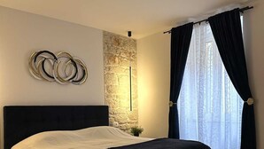 Une chambre moderne avec un lit, un mur décoratif en pierre, une lampe sur pied et une grande fenêtre avec des rideaux.