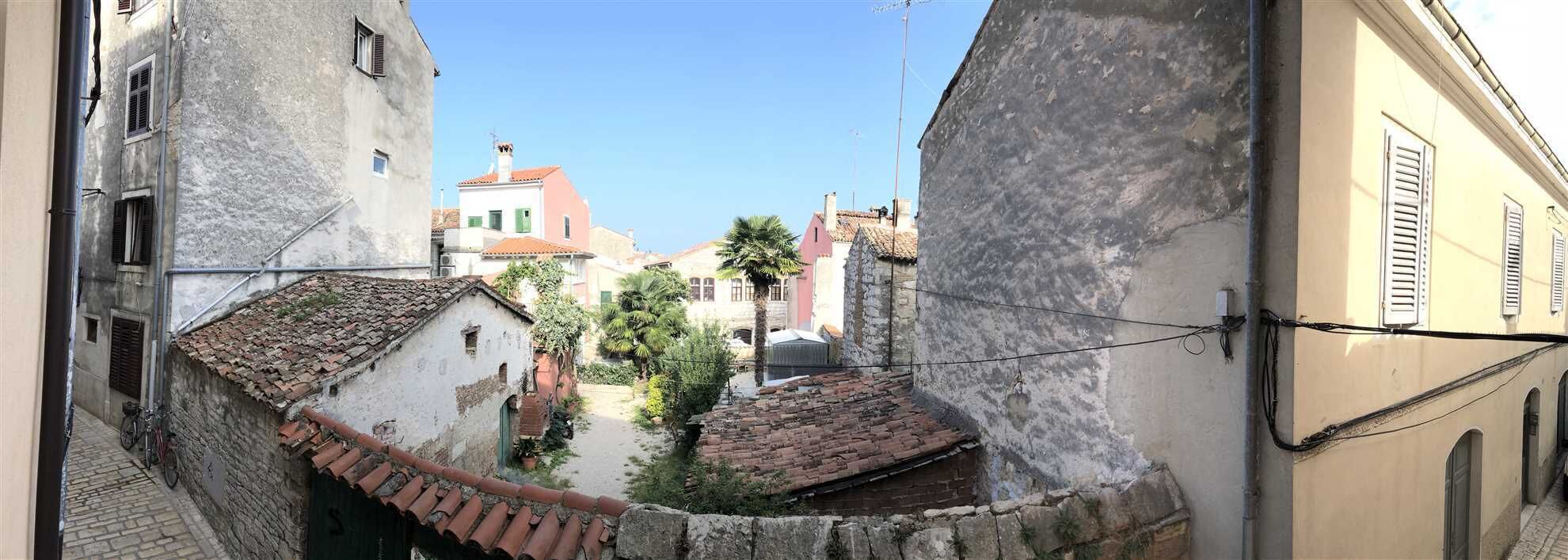 A narrow street with buildings on either side, some with visible windows and shutters.
