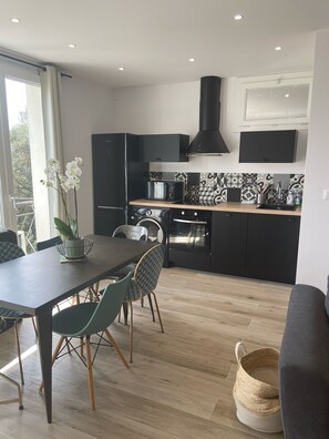 A modern kitchen with black cabinetry, a microwave, and a built-in oven. There is a dining table with chairs and a potted plant.