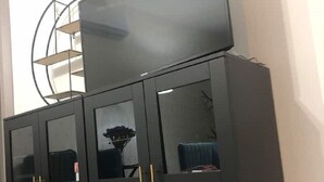 Een zwarte kast met glazen deuren en gouden handgrepen, geplaatst in een kamer met een witte muur en een rond metalen schap in de achtergrond.
