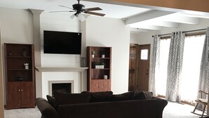 Een woonkamer met een donkerbruine bank, houten kasten, een flatscreen televisie en een open haard.
