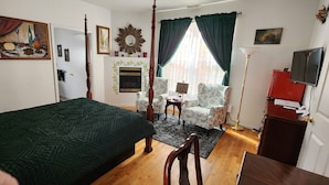 A bedroom with a four-poster bed, a sitting area with two chairs, a television, and a fireplace. - Happy Days and Nights - Valiant (Harbor Springs)
