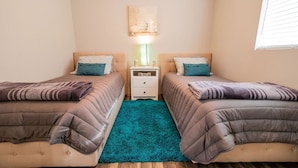 Un dormitorio con dos camas, un tapete color turquesa y una mesita de noche con lámpara.