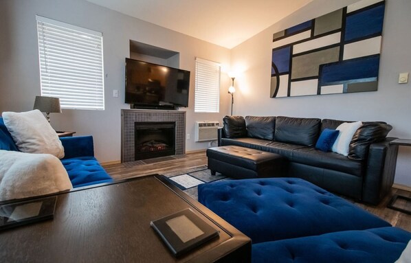 Een moderne woonkamer met een open haard, een flatscreen-tv en een groot abstract schilderij aan de muur.