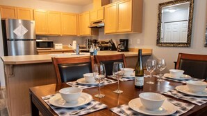 Comedor con mesa de madera dispuesta para cuatro, con cuencos blancos, copas de vino y una botella de vino.