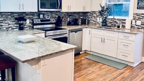 Una cocina moderna con armarios blancos, encimera de granito, microondas integrado y una isla grande con asientos tipo barra.