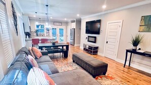 Un salón comedor amplio con un sofá modular grande, una zona de estar con lámpara de araña y un televisor montado en la pared.