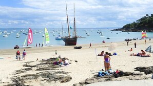 Ein Strand mit Booten, Menschen und einer Segelyacht im Wasser.