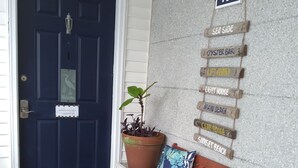 Un banc en bois avec un coussin coloré, une plante en pot et une porte sur laquelle est apposée une plaque indiquant le numéro 406.