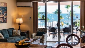Habitació d'hotel amb un balcó que domina l'oceà, que disposa d'un sofà, cadires, una taula de menjador i una làmpada.