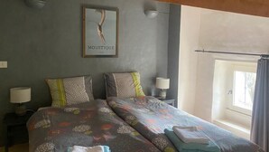 A bedroom with two beds, a framed picture on the wall, and a window with curtains.