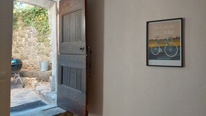 A rustic wooden door leading to a stone-walled courtyard with a bicycle and a grill.