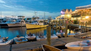 A marina with various boats docked, a wooden dock, and a building with a balcony. - Cozy Beach Cottage (Oak Bluffs)