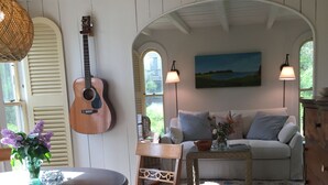 A cozy room with a wooden ceiling, a dining table with chairs, a guitar, a sofa, and a painting on the wall. - Cozy Beach Cottage (Oak Bluffs)