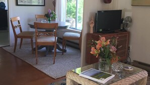 A cozy living room with a wooden dining table, chairs, a sofa, a TV, and a guitar on the wall. - Cozy Beach Cottage (Oak Bluffs)