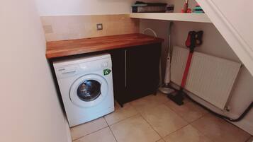 Ein kleiner Hauswirtschaftsraum mit Waschmaschine, Heizkörper und Besen.