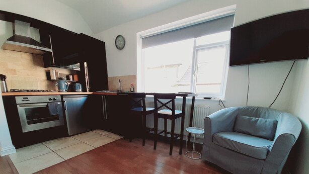 Una cocina compacta con electrodomésticos modernos, un área de comedor con mesa y sillas, y un sofá gris.