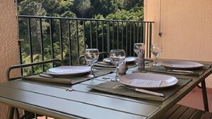 Ein Balkon mit Tisch, Geschirr, Gläsern und Besteck, mit Blick auf einen bewaldeten Hang.