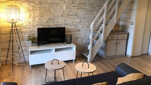 Ein modernes Wohnzimmer mit einer Steinwand, einer weißen Unterhaltungseinheit, einem schwarzen Sofa, zwei kleinen Tischen und einer Treppe.