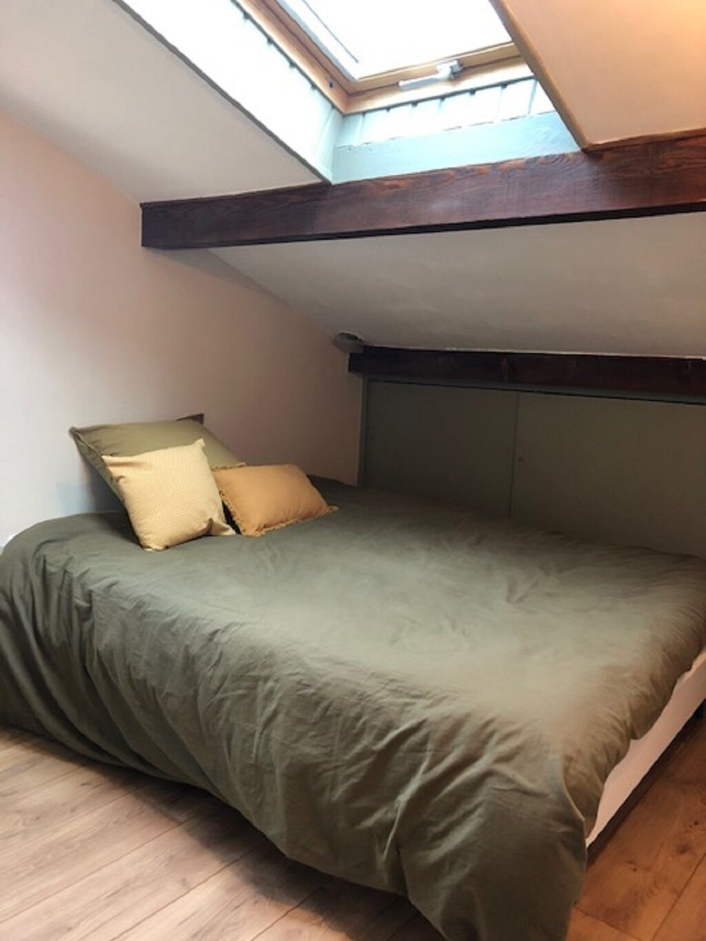 Habitación con techo inclinado y tragaluces, con cama y ropa de cama verde y dos almohadas.