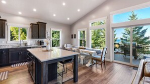 Una cocina amplia con una isla grande, armarios de madera oscura y vistas al exterior a través de ventanas panorámicas.