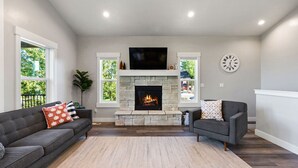 Una sala de estar con chimenea de piedra, dos sofás, un televisor y un reloj en la pared.