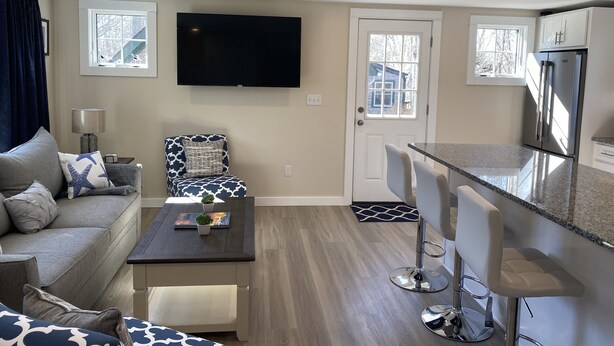 A modern living room with a sofa, a coffee table, and a TV. There is a kitchen area with a refrigerator and bar stools. - Private home, short walk to Harbour Island beach! Central A/C, family friendly! (Narragansett)