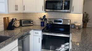 A modern kitchen with white cabinets, stainless steel appliances, a granite countertop, and a wooden floor. - Private home, short walk to Harbour Island beach! Central A/C, family friendly! (Narragansett)