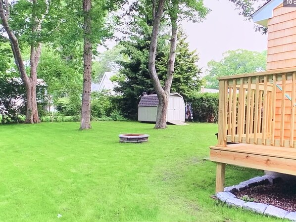 A backyard with a wooden deck, a circular stone feature, and a shed in the background. - Private home, short walk to Harbour Island beach! Central A/C, family friendly! (Narragansett)