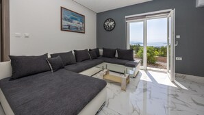 Ein modernes Wohnzimmer mit einem grauen Ecksofa, einem Glastisch, einer Weltzeituhr und einem Gemälde an der Wand.