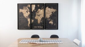 Un coin repas avec une table en bois, trois cartes du monde encadrées et deux chaises.