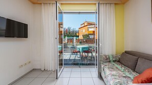 A balcony with a glass door, a sofa, and a TV on the wall. - Lovely apartment in Umag with WiFi (Umag)
