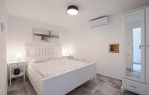 A bedroom with a white bed, bedside lamps, a ceiling light, a wall-mounted air conditioner, and a wardrobe. - Cozy home in Donji Prolozac (Donji Prolozac)